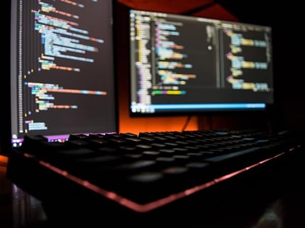 keyboard with two monitors showing blurred out code